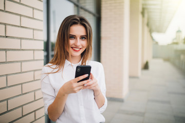 Young pretty woman use mobile phone in her hands in front of a commercial building