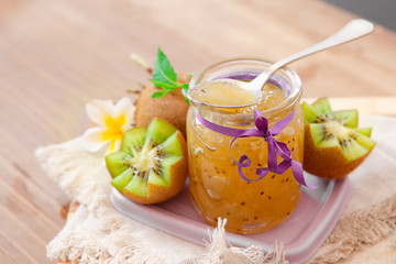 Exotic kiwi jam with ripe fruits on wooden background