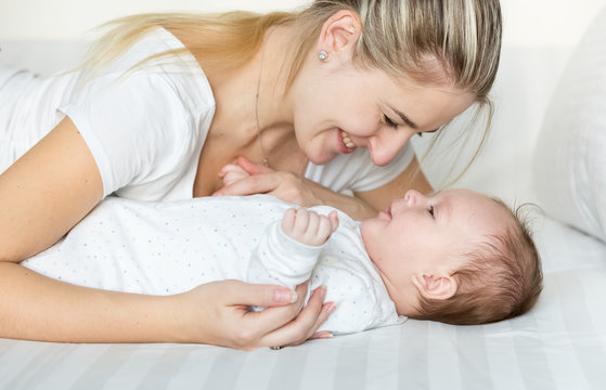 Portrait of adorable baby and smiling young mother lying on bed and looking at each other