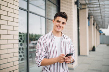 Man texting on phone. Casual urban professional entrepreneur using smartphone smiling happy outside office building. Outdoor portrait of modern young guy with mobile in the street