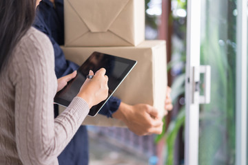 Fast and reliable service. Young woman signing on tablet pc computer at the entrance of her home. delivery man giving delivering parcel box.