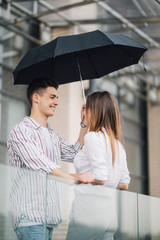 Young couple of lovers under a umbrella in city. Handsome people having fun in city urban center in a raining day. Love and vacation concept