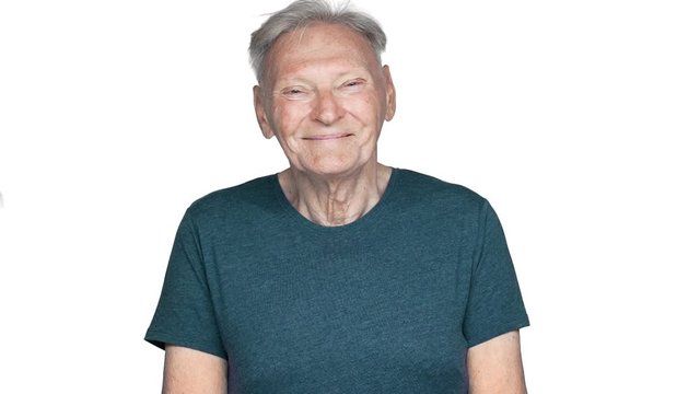 Portrait of kind and cheerful old aged man 80s having gray hair in basic t-shirt looking at camera with smile in slow motion, isolated over white background