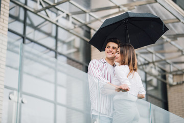 Young couple of lovers under a umbrella in city. Handsome people having fun in city urban center in...