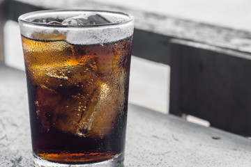 Glass of cola with ice on wooden table., with blur river outdoor background., hot concept. thirsty concept.