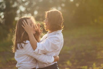 a woman with a daughter as a teenager huggingon the nature in the soft sunset light