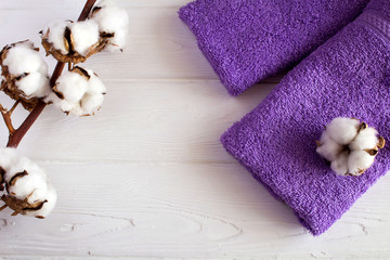 Branch of cottton and violet  towels on the  white wooden  background.Top view.