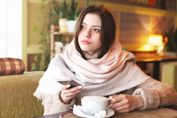 Beautiful young girl enjoys phone in cafe
