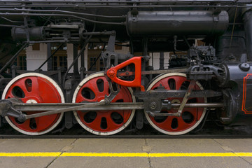 fragment of vintage functioning steam locomotive standing at station, closeup, visible driving wheels with a system of pistons, connecting rods and levers
