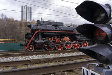 vintage locomotive leaves because of a traffic light in the foreground on the modern railway station