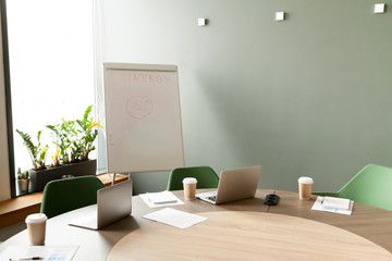 Conference table with laptops and chairs in empty meeting room with nobody, modern company office boardroom interior with flip chart for daily work and corporate team group business briefings concept