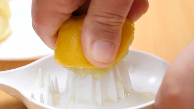 Male hand squeezing fresh lemon fruit using plastic juice squeezer. Making healthy citrus sour drink. Slow motion