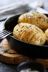 Close-up of homemade baked potato with olive oil, garlic, rosemary, mustard, dill and black pepper in a cost fry pan.