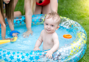 Portrait of happy smiling toddler boy having fun in inflatable swimming pool with family