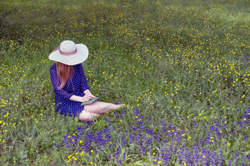 Fototapeta na wymiar girl in blue dress and white hat ,sitting on the grass, holding a sketchbook