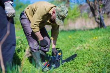Obraz premium rustic man is repairing a chainsaw. Start the engine.