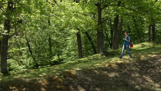 Woman with backpack walking on forest edge enjoying the shade in the sunny spring nature