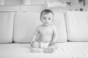 Black and white photo of sad baby boy indiapers sitting on sofa