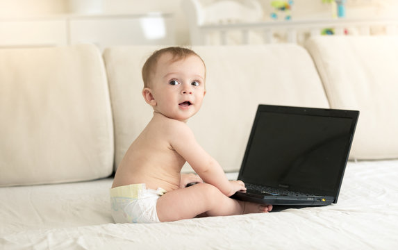 Toned portrait of cute baby boy sitting on sofa and using computer