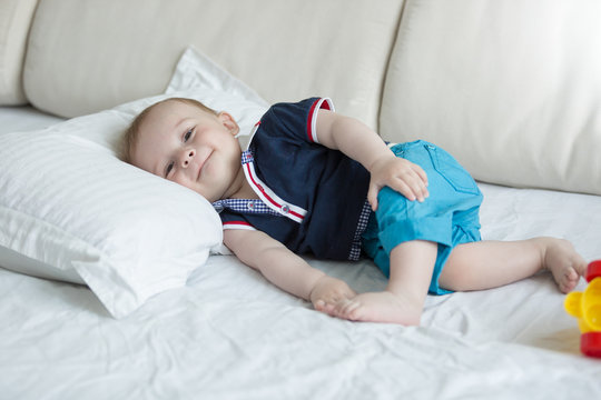 Cute smiling baby boy lying on bed and looking in camera