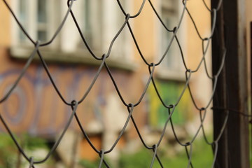Fototapeta premium Metal Mesh Fence Fragment Foreground And Graffiti Wall Background City Sofia Bulgaria.