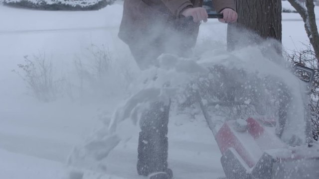 Man pushing snow blower from the front, shooting snow to the side. Slow motion (120fps at 24)