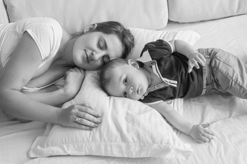 Black and white high point view photo of young mother sleeping next her baby boy lying in bed