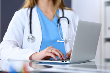 Doctor typing on laptop computer while sitting at the glass desk in hospital office. Physician at work. Medicine and healthcare concept