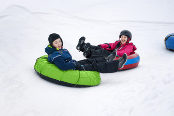 Fototapeta na wymiar Kids on snow tubes downhill at winter day.