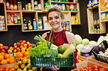 Girl in red holding different vegetables on fruits store.