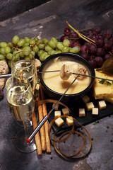 Gourmet Swiss fondue dinner on a winter evening with assorted cheeses on a board alongside a heated pot of cheese fondue