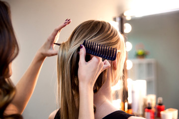 Fototapeta premium Hairstylist combs client's light-brown with blonde hair. Creating a luxurious evening hairstyle with ringlets of medium length.