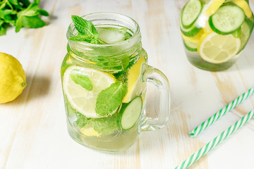 Detox water infused with sliced lemon, cucumber and sprigs of mint on wooden background.