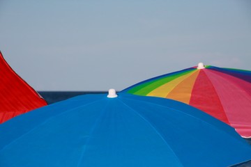 Red, Blue and Multi-Colored Umbrellas on the Beach with the Sea and Clear Blue Sky in the Background