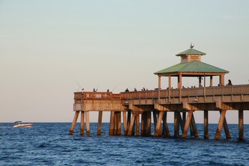 Boat Passing by the Deerfield Beach, Florida Pier with People Fishing in the Late Afternoon Sun Beneath a Clear Blue Sky