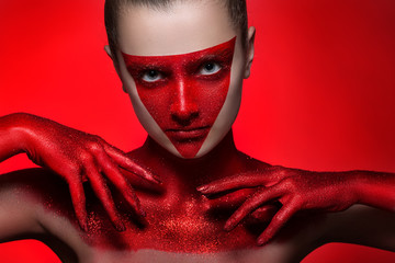beauty fashion portrait of a young girl. Face and hands painted with red paint with glitter. the Red particles of the metal powder. tinsel
