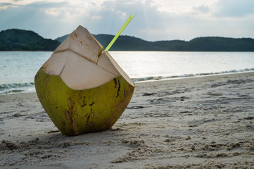 Cocktail in coconut on sandy beach at sunset