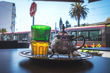 Obraz premium a glass of moroccan tea and tea pot in a coffee shop terrace and a tram passing behind