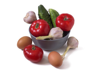Cucumbers, garlic, tomatoes and two brown eggs. Vegetables in a gray bowl and around it isolated on a white background