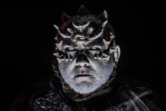 Alien, demon, sorcerer makeup. Horror and fantasy concept. Man with third eye, thorns or warts. Demon on black background, close up. Senior man with white beard dressed like monster in darkness.