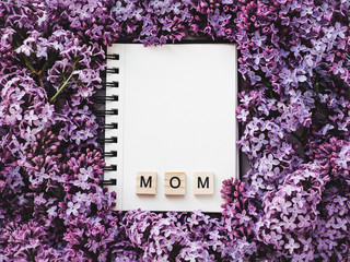 Notepad with the word MOM and a blank page for Your inscription on the background of blossoming flowers. Top view, close-up. Congratulations for relatives and loved ones. Concept of a happy family