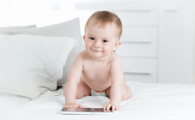 Fototapeta premium Portrait of smiling baby boy in diapers crawling towards digital tablet computer and looking in camera