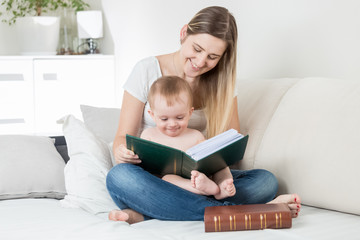 Beautiful young smiling mother readin stories to her baby boy on bed