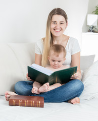 Portrait of cute baby boy sitting on mothers lap and reading big book