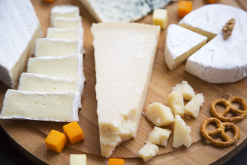 Delicious cheese with pretzels and walnuts on wooden board, closeup. Food for wine.