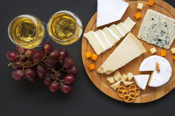 Tasting delicious cheese with wine, grapes, pretzels and walnuts on dark background, from above.Top view. Flat lay.