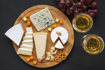 Cheese platter with wine, grapes, pretzels and walnuts on dark background, from above.Top view. Flat lay.