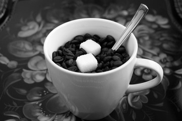 White cup with a spoon coffee beans and two pieces of sugar.