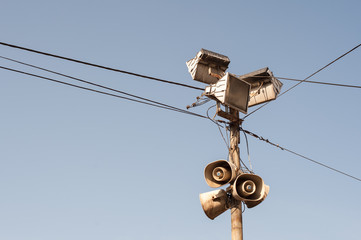 Old outdoor public loudspeakers, megaphones and reflectors on metal pole with black electric cables