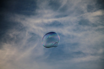 Soap bubble against the background of the blue sky and clouds
